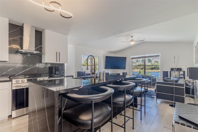 kitchen with a sink, stainless steel range with electric cooktop, dark countertops, wall chimney range hood, and open floor plan