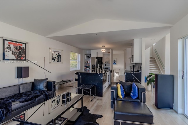 living room featuring stairs, vaulted ceiling, and light wood-style floors