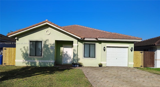 view of front facade with a tile roof, a front yard, stucco siding, decorative driveway, and an attached garage