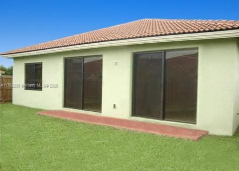 back of property featuring a tile roof, a lawn, and stucco siding