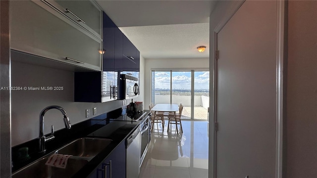 kitchen featuring a sink, dark countertops, a textured ceiling, appliances with stainless steel finishes, and light tile patterned floors