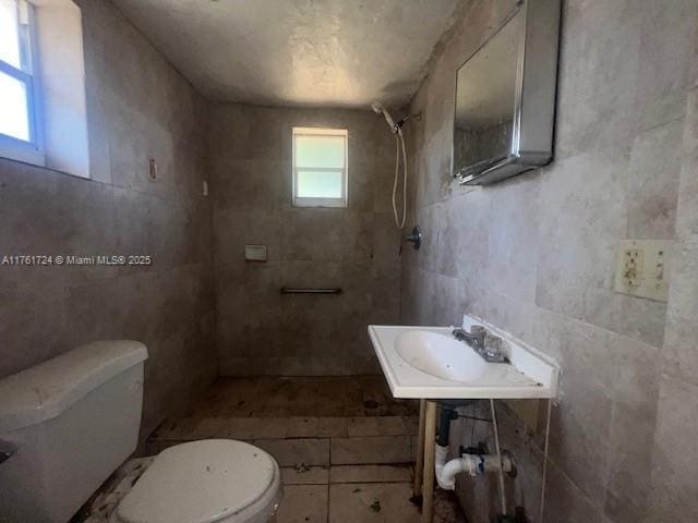 full bath featuring a sink, tiled shower, toilet, and tile walls