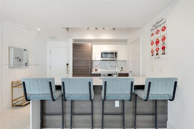 kitchen with stainless steel microwave, a breakfast bar, decorative backsplash, high quality fridge, and white cabinetry