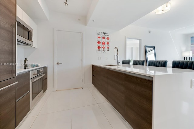 kitchen featuring light countertops, appliances with stainless steel finishes, a kitchen breakfast bar, modern cabinets, and a sink