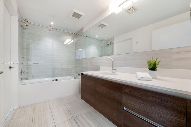 bathroom featuring vanity, tile walls, visible vents, and bath / shower combo with glass door