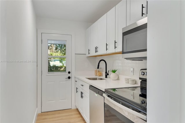 kitchen featuring light wood finished floors, backsplash, stainless steel appliances, white cabinetry, and a sink