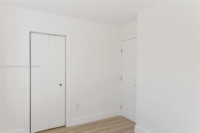 unfurnished bedroom featuring a closet, baseboards, and light wood-style flooring