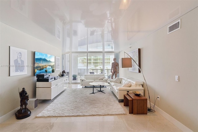 living area featuring visible vents, baseboards, a towering ceiling, and tile patterned flooring