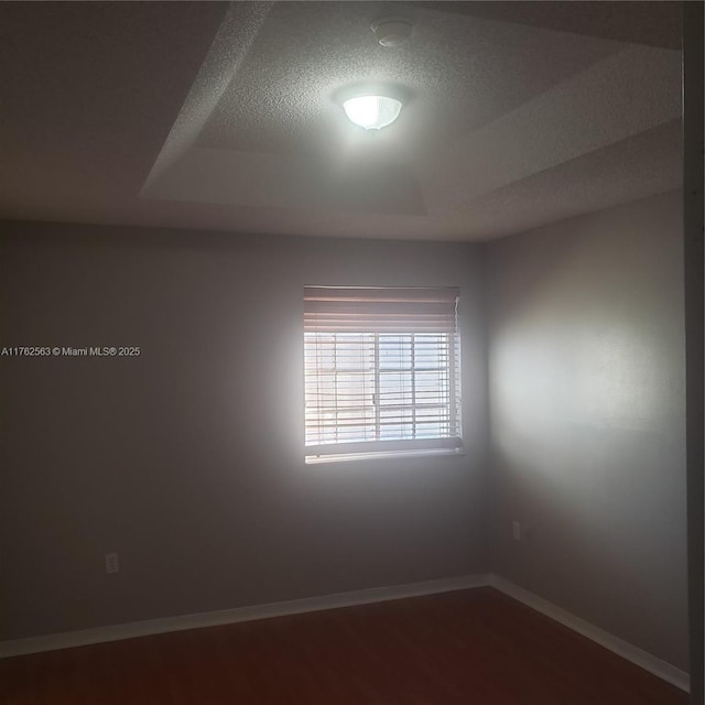 spare room featuring a textured ceiling, baseboards, and dark wood-style flooring