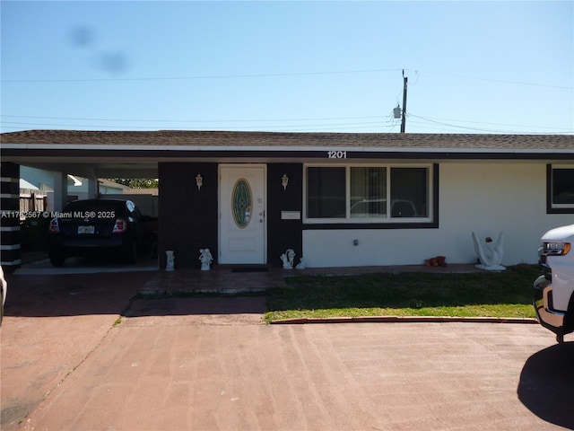 view of front facade with stucco siding, an attached carport, driveway, and a shingled roof