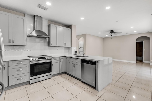 kitchen with wall chimney exhaust hood, arched walkways, appliances with stainless steel finishes, and gray cabinetry