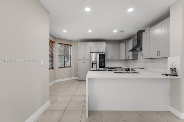 kitchen featuring light countertops, stainless steel fridge with ice dispenser, baseboards, a peninsula, and wall chimney exhaust hood