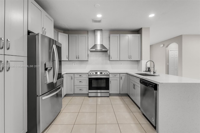 kitchen with a sink, light countertops, wall chimney exhaust hood, stainless steel appliances, and a peninsula