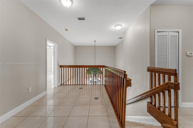 hallway featuring tile patterned flooring, visible vents, a textured wall, baseboards, and an upstairs landing