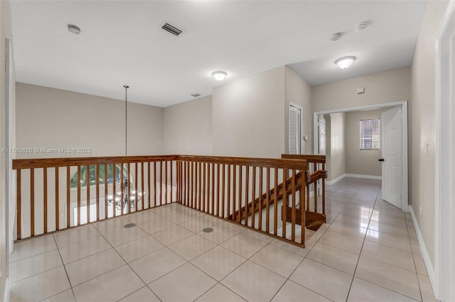 hall with baseboards, visible vents, light tile patterned floors, and an upstairs landing