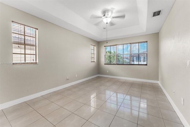 empty room with a ceiling fan, visible vents, light tile patterned floors, a raised ceiling, and baseboards