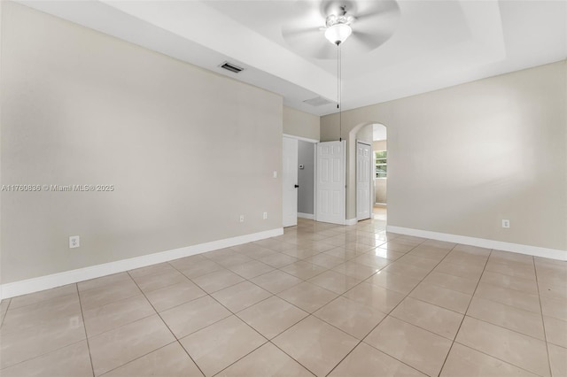spare room with visible vents, ceiling fan, a tray ceiling, arched walkways, and light tile patterned floors