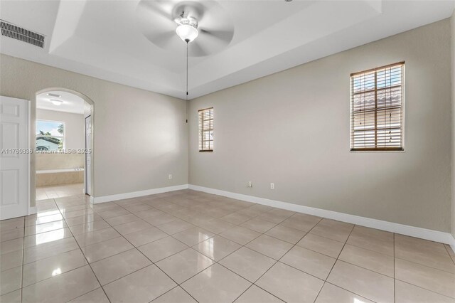empty room featuring ceiling fan, visible vents, arched walkways, a tray ceiling, and light tile patterned flooring