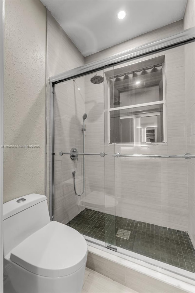 full bathroom featuring a shower stall, toilet, and a textured wall