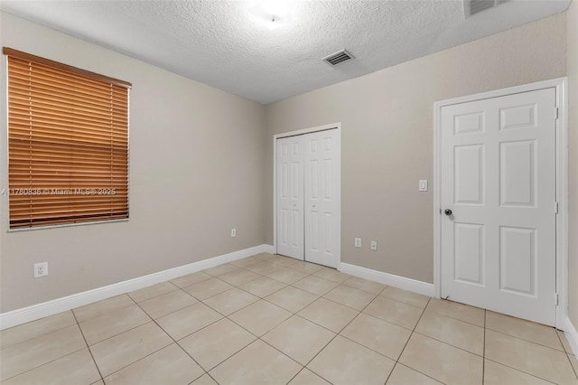 unfurnished bedroom with a textured ceiling, light tile patterned flooring, and visible vents