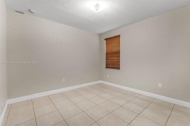 spare room featuring light tile patterned floors, baseboards, and a textured ceiling