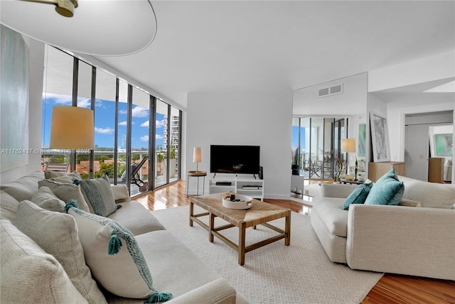 living room with floor to ceiling windows, plenty of natural light, wood finished floors, and visible vents