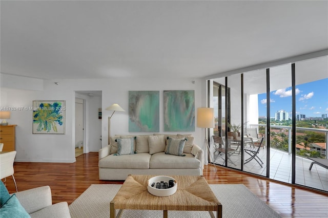 living room featuring a city view, a wall of windows, baseboards, and wood finished floors