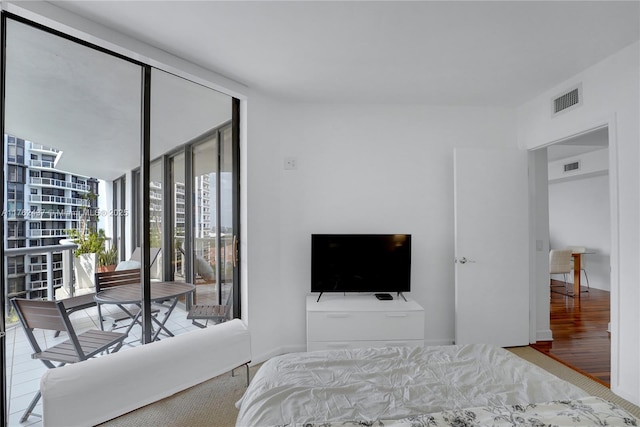 bedroom with visible vents, wood finished floors, a wall of windows, and access to outside