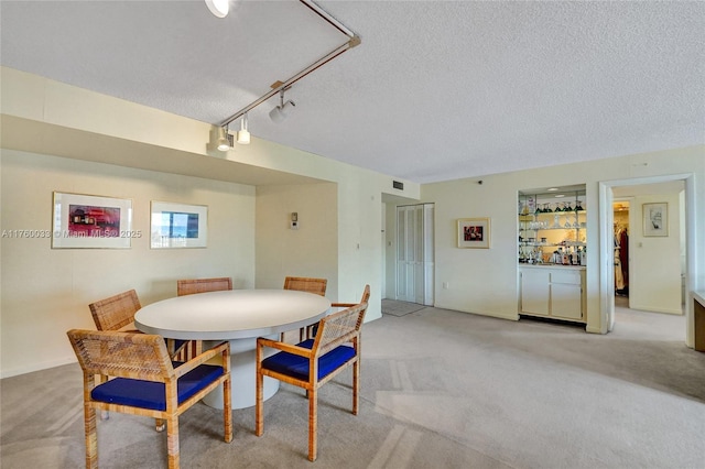 carpeted dining room featuring a bar, rail lighting, visible vents, and a textured ceiling