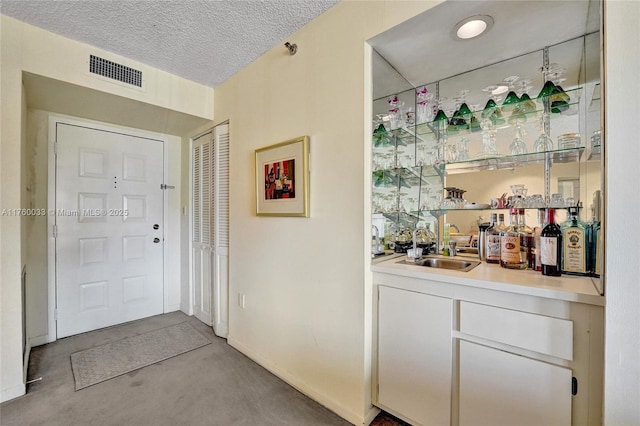 interior space featuring visible vents, a textured ceiling, wet bar, and concrete flooring