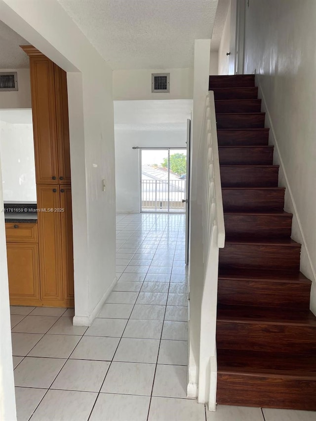 stairs featuring tile patterned floors, visible vents, a textured ceiling, and baseboards