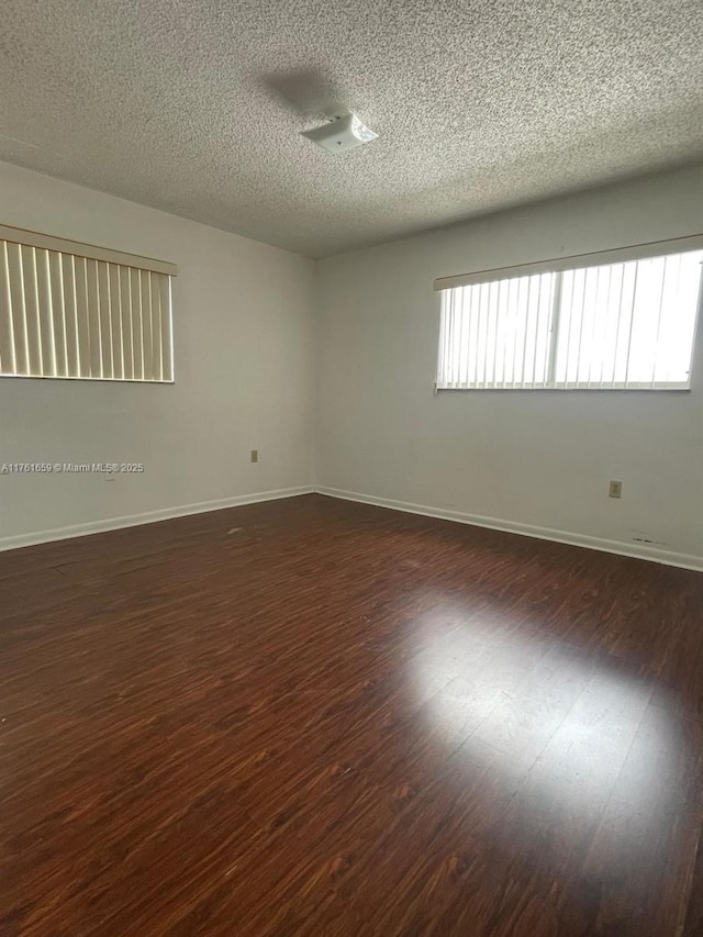 unfurnished room with dark wood finished floors, plenty of natural light, and baseboards