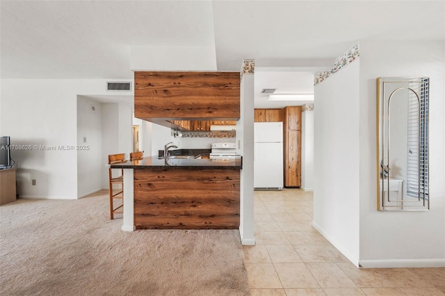 kitchen featuring baseboards, a breakfast bar area, light tile patterned floors, white appliances, and a sink