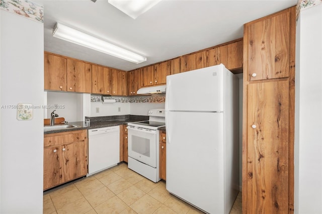 kitchen with a sink, under cabinet range hood, dark countertops, white appliances, and light tile patterned floors