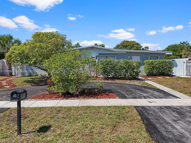 view of front facade featuring aphalt driveway, stucco siding, a front lawn, and fence