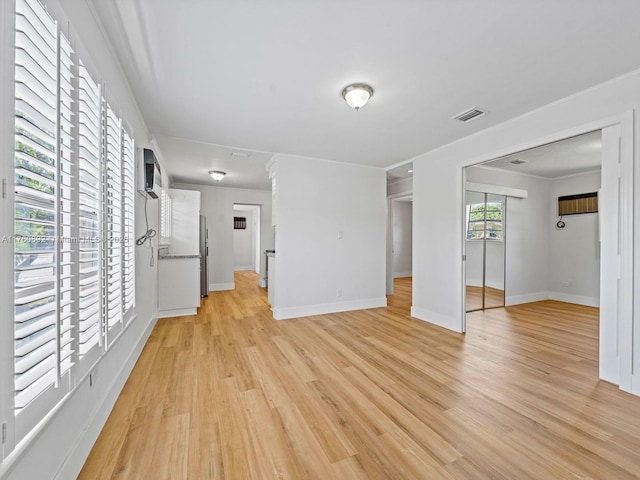 unfurnished living room featuring visible vents, crown molding, light wood-type flooring, and baseboards