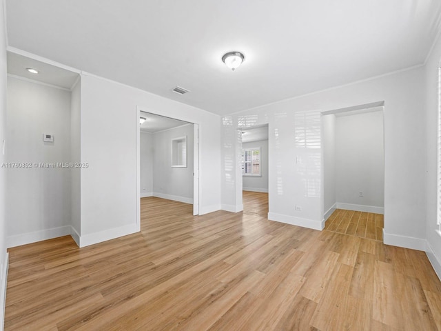 empty room with ornamental molding, baseboards, visible vents, and light wood-type flooring