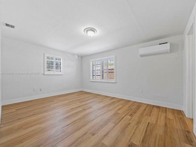 unfurnished room featuring visible vents, baseboards, a wall mounted AC, and light wood-style floors