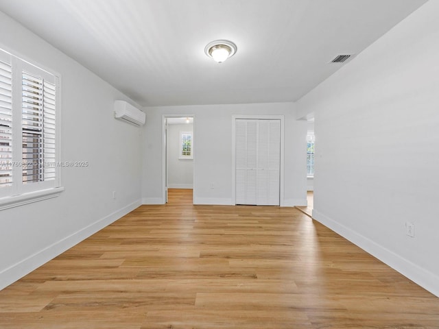 unfurnished room with visible vents, a wall mounted air conditioner, light wood-type flooring, and baseboards