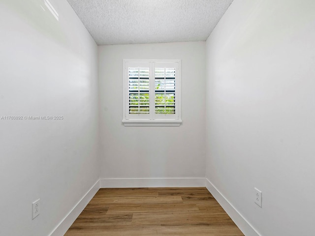 spare room with light wood-style flooring, a textured ceiling, and baseboards