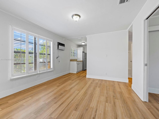 unfurnished living room featuring a wall unit AC, baseboards, visible vents, and light wood finished floors