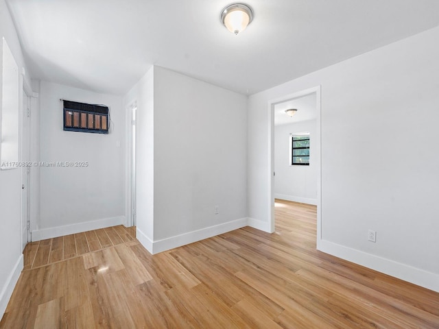 spare room with baseboards and light wood-style floors