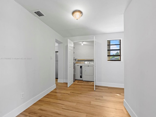 corridor with light wood-type flooring, visible vents, baseboards, and washing machine and clothes dryer