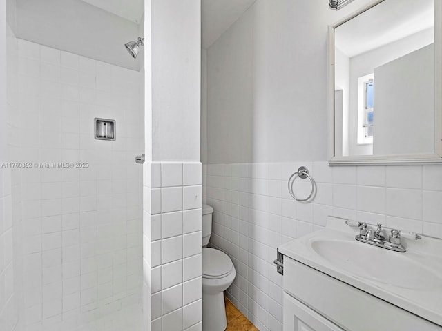 full bathroom with a tile shower, vanity, toilet, and tile walls