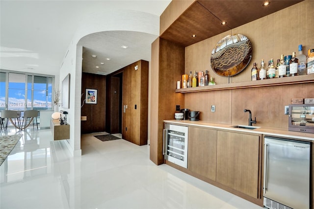 bar featuring beverage cooler, arched walkways, a sink, indoor wet bar, and stainless steel fridge