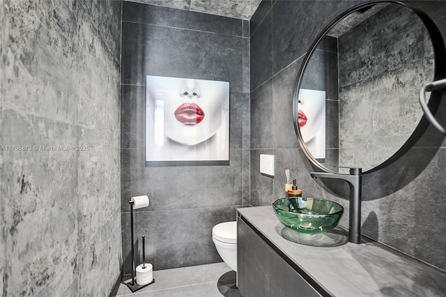 half bath with tile patterned flooring, toilet, vanity, and tile walls