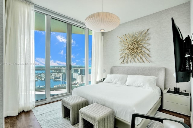 bedroom featuring a wall of windows, wood finished floors, access to exterior, and a water view