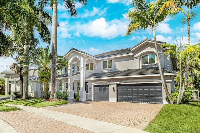 view of front of property with decorative driveway, a front lawn, an attached garage, and stucco siding