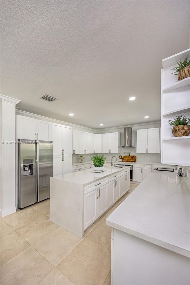 kitchen with an island with sink, stainless steel fridge, white cabinetry, wall chimney exhaust hood, and open shelves