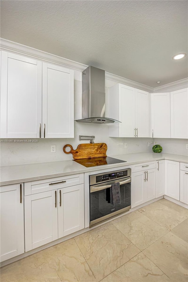 kitchen featuring stainless steel oven, wall chimney exhaust hood, and white cabinets